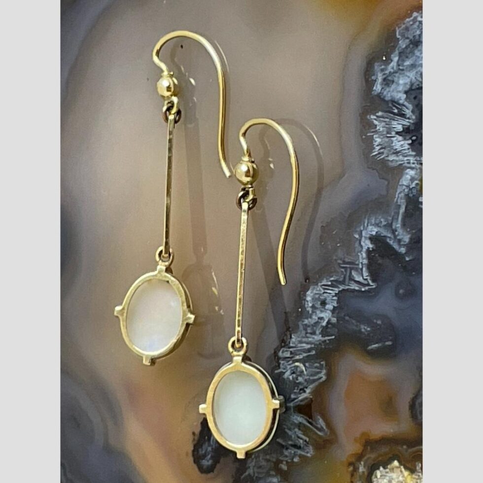 Photo of the earrings again displayed on a slice of natural agate this time with the back on display showing the opal setting.