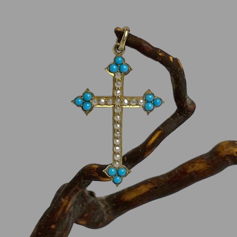 Main photo of antique 18Kt gold cross displayed hanging from a twig from a cherry tree by its bail. This petite antique cross has arrow head tips set with 3 sleeping beauty turquoise stones and seed pearls lining the rest of the cross. A fine gold chain would be ideal for this cross.