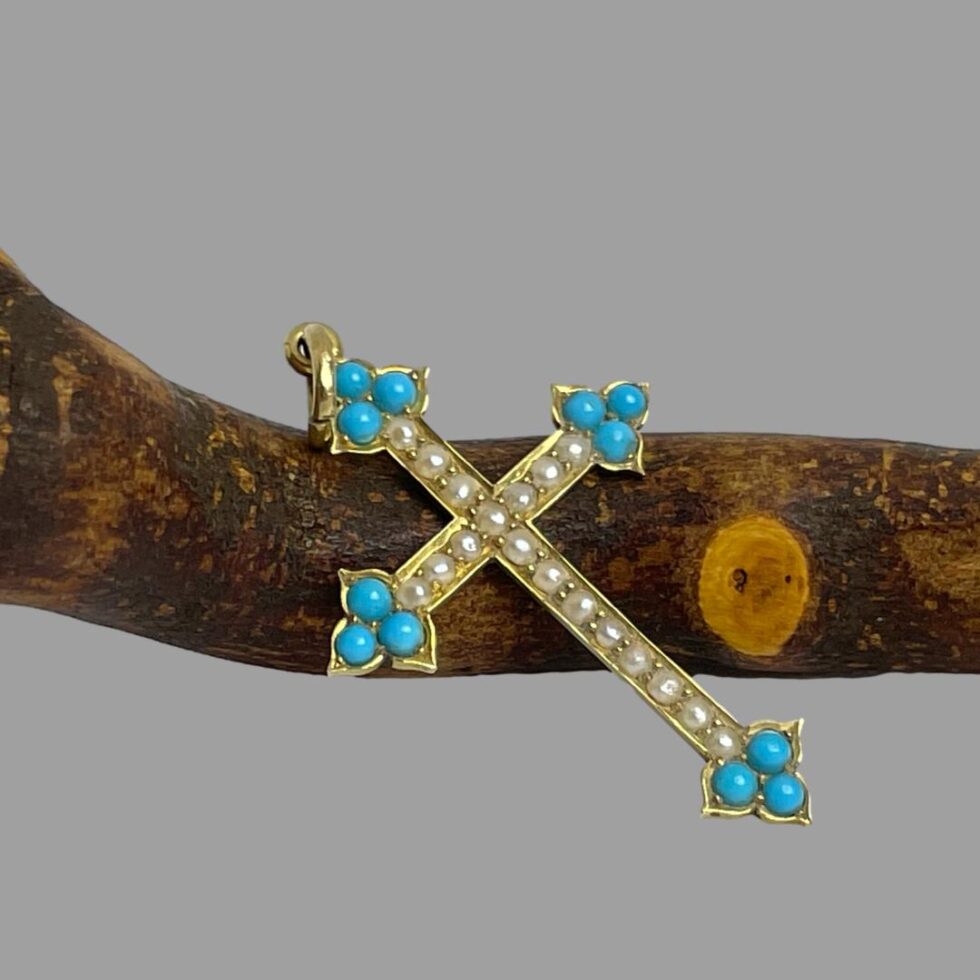 Photo of antique 18Kt gold cross displayed leaning diagonally against the cherry tree twig with the cross front facing upward towards the top right corner of photo. The light is catching the seed pearls.