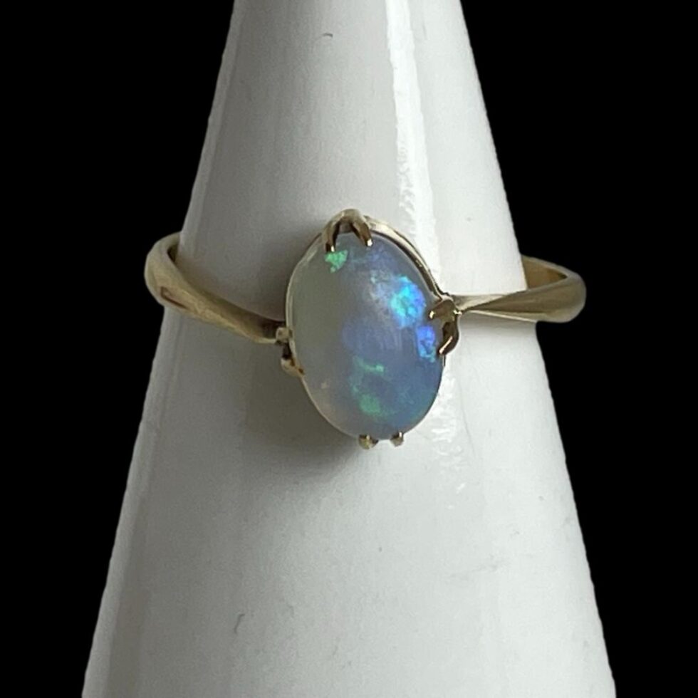 Photo of 9 karat gold opal ring displayed on a cone shaped stand with the ring front forward facing. The uneven band is well displayed here with shoulder on left lower than right and the top of the oval opal leaning in slightly to the left at top.