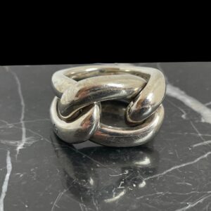 Main photo of Pomellato gourmet knot ring displayed on top of a block of black marble and the ring front forward facing. The ring appears like a rope knot but is in fact 2 pieces of tubular silver. One piece makes up the band and shoulders - imagine a rubber band that has been set in silver and moulded into a solid form. The front of the ring is a separate smaller tubular band that has been weaved within the main band to create a knot look.