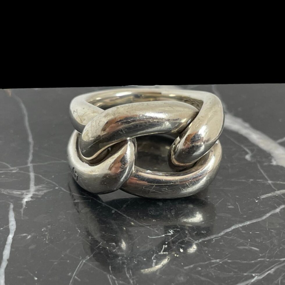 Main photo of Pomellato gourmet knot ring displayed on top of a block of black marble and the ring front forward facing. The ring appears like a rope knot but is in fact 2 pieces of tubular silver. One piece makes up the band and shoulders - imagine a rubber band that has been set in silver and moulded into a solid form. The front of the ring is a separate smaller tubular band that has been weaved within the main band to create a knot look.