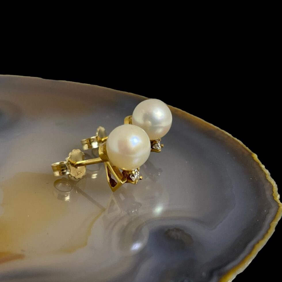 Photo of gold pearl diamond studs still on the agate slice and seen from a side angle with the earring fronts facing right