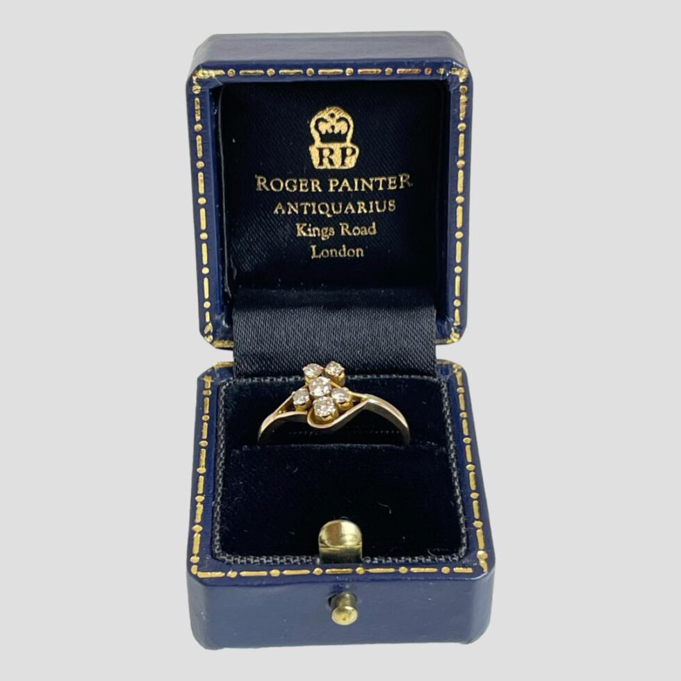 Main photo of gold diamond flower ring displayed inside its vintage ring box (included) which is open from the front.The ring has an interesting and unusual design with 6 diamonds set with largest in the centre with a smaller one to its left (in this photo) next largest is below the central one with a smaller one to its right and at the top are 2 small ones side by side above the large central one.