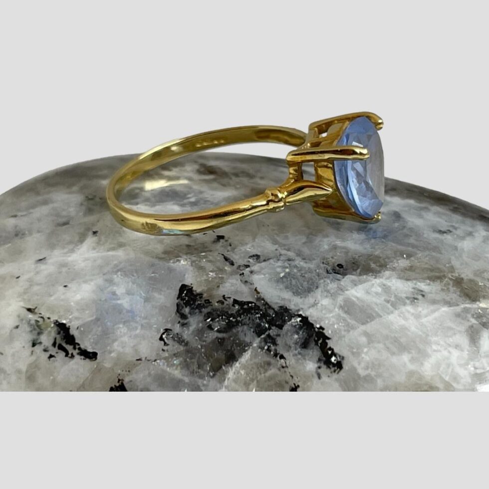 Photo of ring displayed on top of a smooth rock of natural moonstone with the ring front facing to the right.