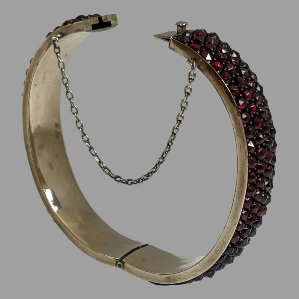 Photo of bracelet stood upright with clasp undone, The safety chain is hanging in a U shape at the opening and the hinge area of bracelet is visible at the centre bottom.