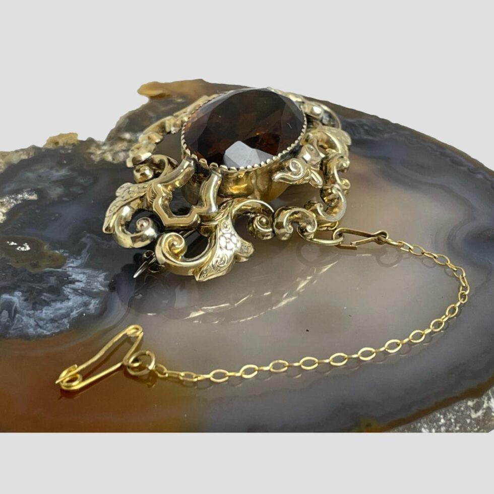 Photo of brooch still on top of the agate slice this time showing it from a slight side angle . The pin of the safety chain is in the foreground