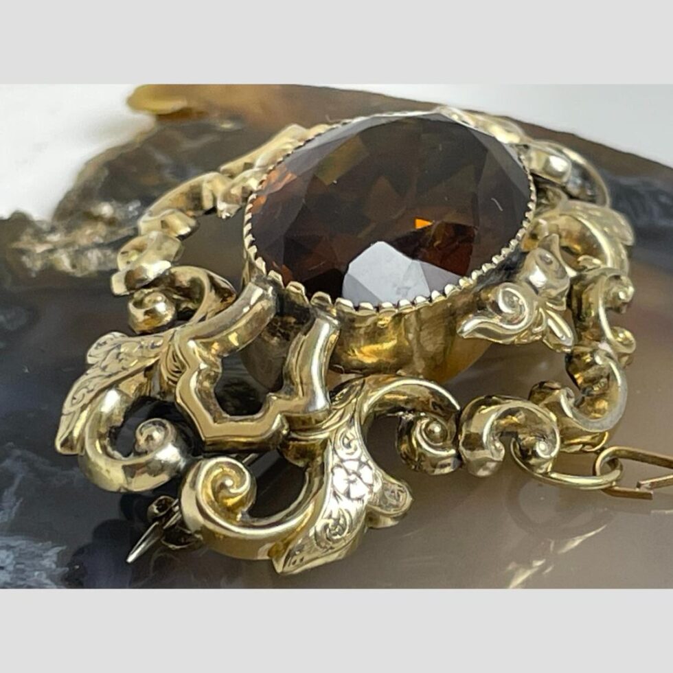 A close up of the brooch from a side angle showing the floral detailing on the gold filled scroll frame.