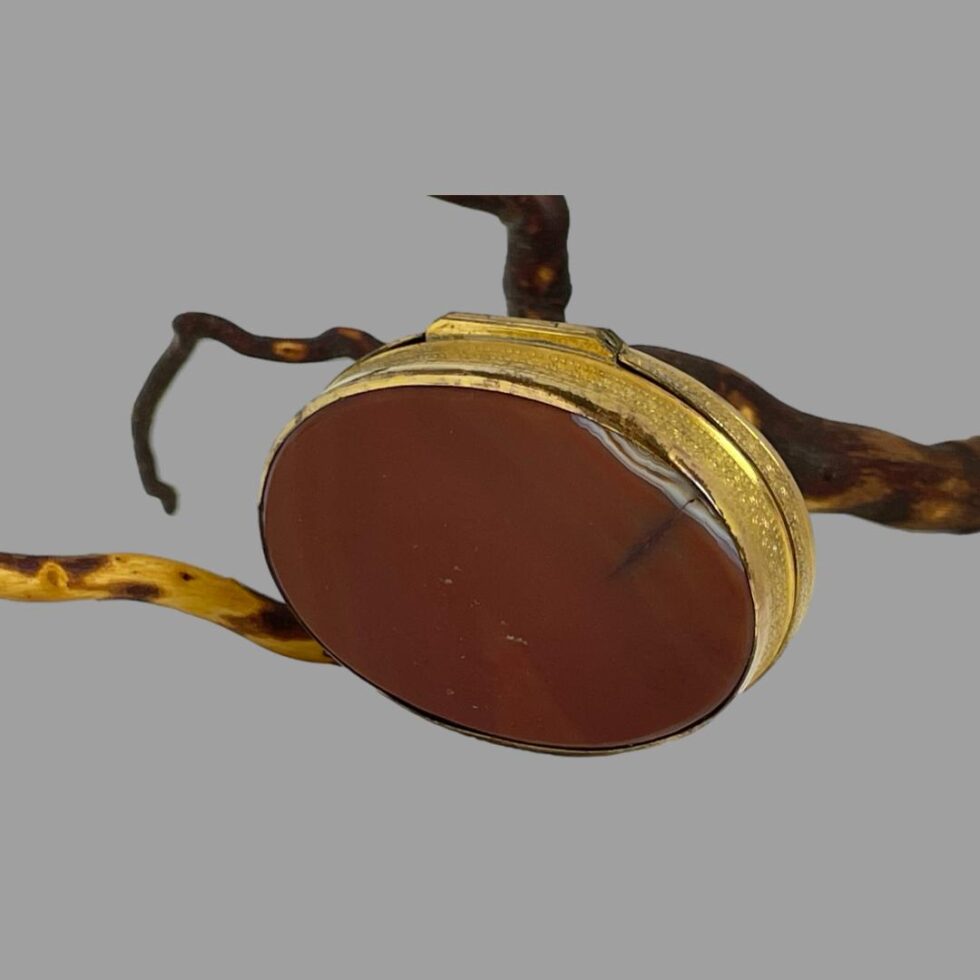 Photo of box leaning against a twig this time with the base agate on display. The agate on the base is a deep terracotta red with lighter patches. The small split in the agate is visible on the right and the hinge side is at the top.
