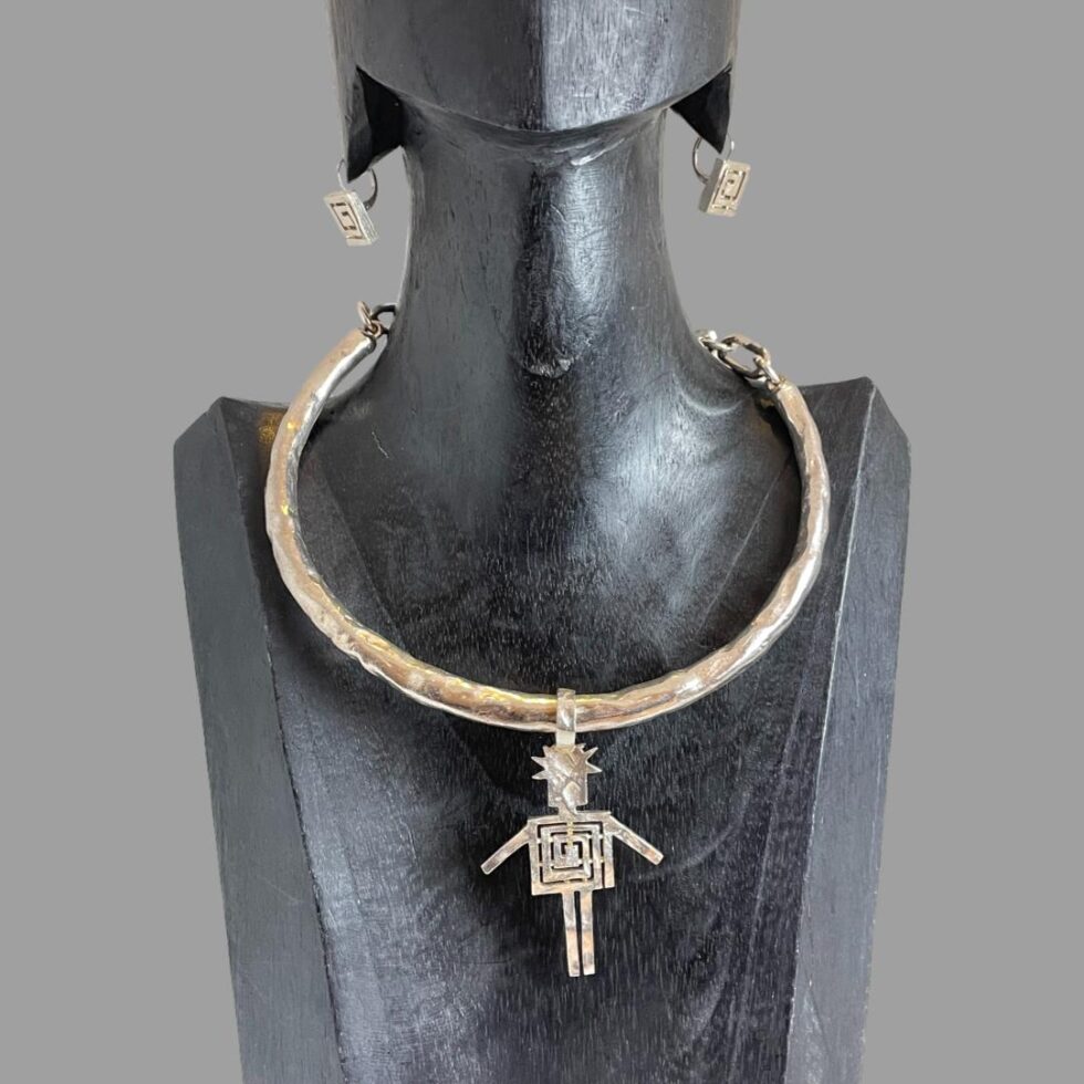 Main photo of Biche de Bere set displayed on a dark wooden display stand and shown forward facing. The earrings are in the lobes of the display and the choker with large pendant is front facing.