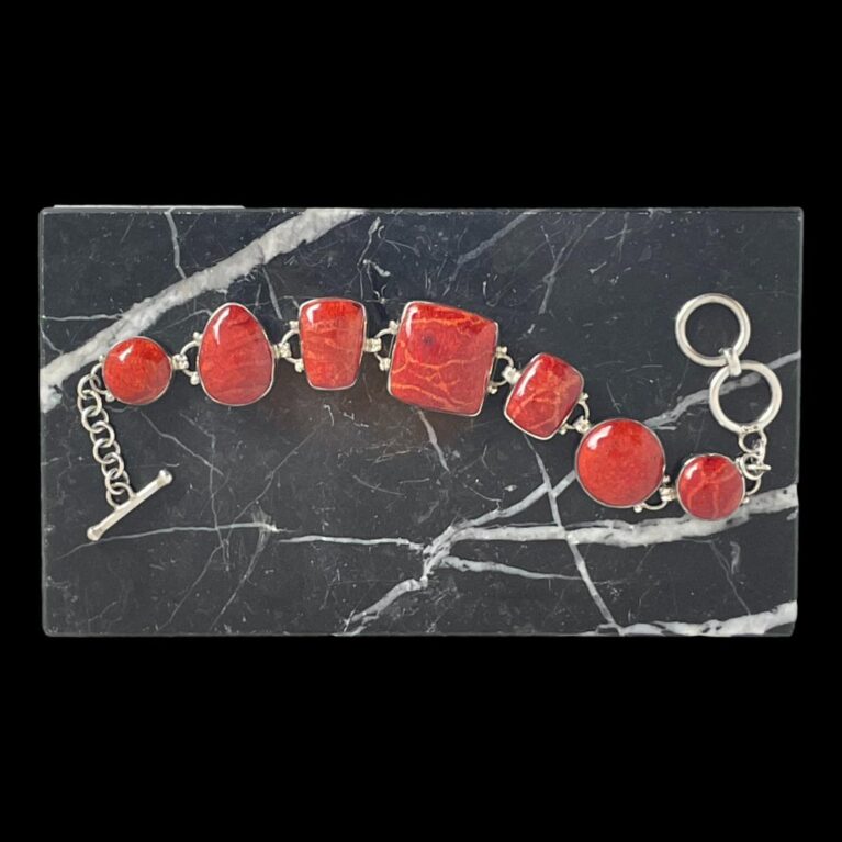 Main photo of red jasper silver bracelet displayed on top of a block of black marble with white inclusions. The bracelet is laid horizontally across in a wave across the marble with the toggle end of clasp on the left and ring end of clasp on the right. The different shapes of the red jasper gives a quirky touch to this chunky bracelet.