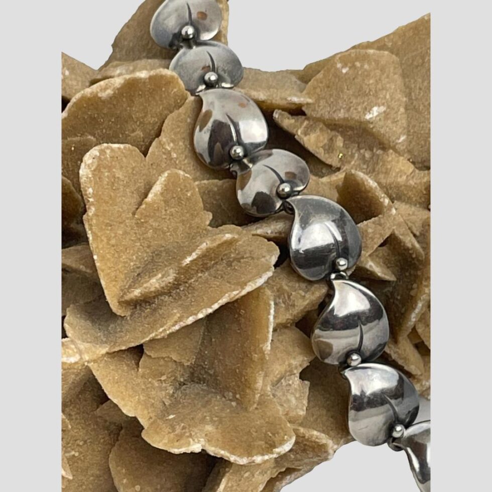 Close up photo of some of the panels of the bracelet still on top of the desert sand rose. The panels are a leaf or heart shape with a small silver ball separating each.