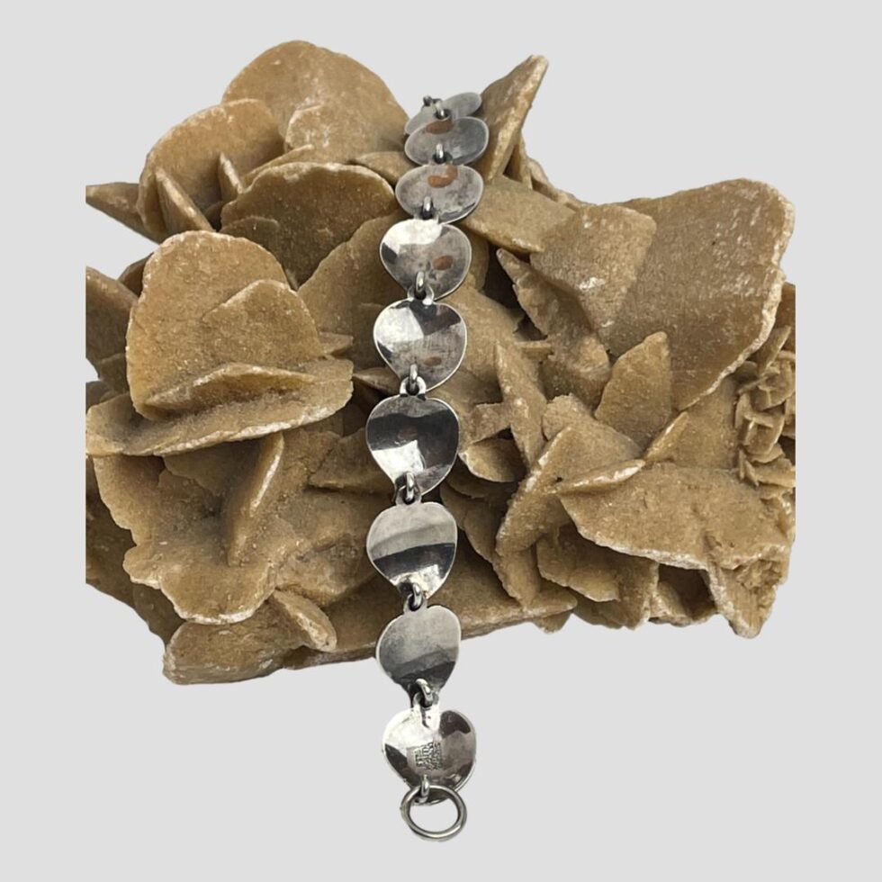 Photo of bracelet displayed with the inside out across the desert sand rose. The hallmark is visible to the panel in the foreground.