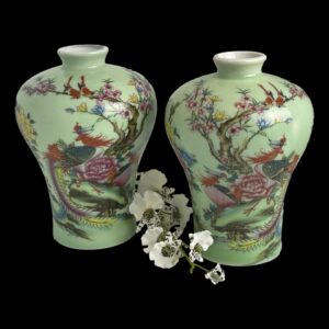 Main photo of Chinese famille rose vases displayed side by side against a black background with a spray of white orchids between them. The main colour of the vases is like a celadon green (a pale minty green) and the decorations are in vibrant colours of red, pink, yellow, blue amongst others depicting exotic birds in a floral setting. The images are mirrored.