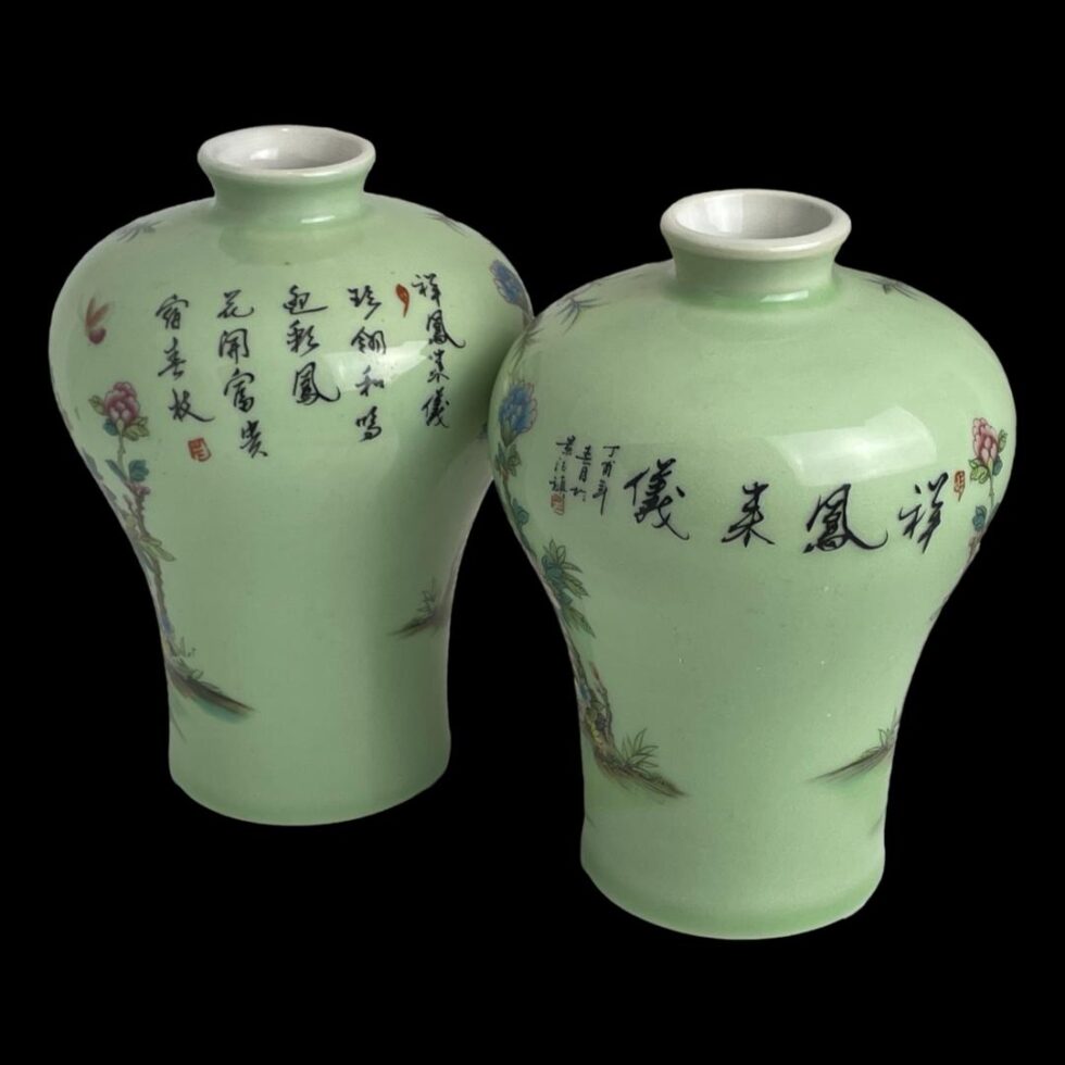 Photo of the back of the vases which have Chinese writing on. The vase on the left has several vertical rows of writing whilst other has one line. Believed to be manufacturing city and artists name.