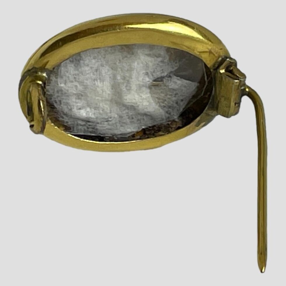 Photo of locket brooch displayed upright with pin open. The pin is pointing straight back and is being used to prop up the brooch.