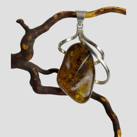 Main photo of pendant shown displayed hanging from a twig and forward facing. The amber piece has a frame in silver with 3 silver swirls extending out & upward to the solid bail. Very unusual silver setting with a modernist feel.