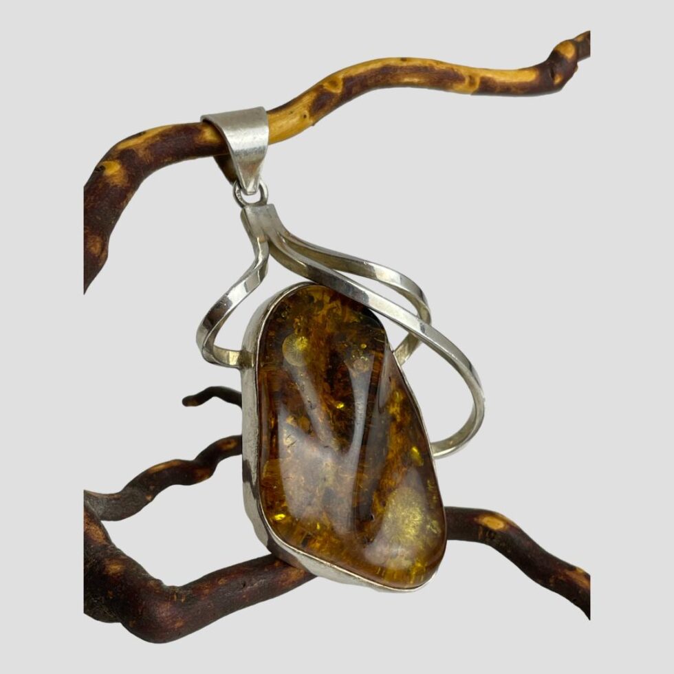Photo of amber pendant still displayed hanging on a twig of cherry and seen from a very slight side angle with the pendant front facing to the right.