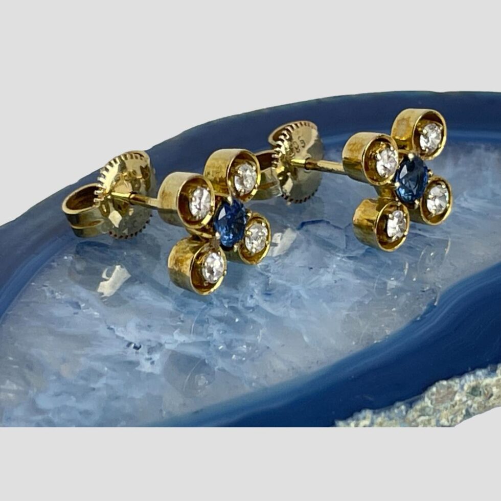 Photo of white &blue sapphire studs still displayed on a slice of blue agate this time with the earring fronts facing to the right.