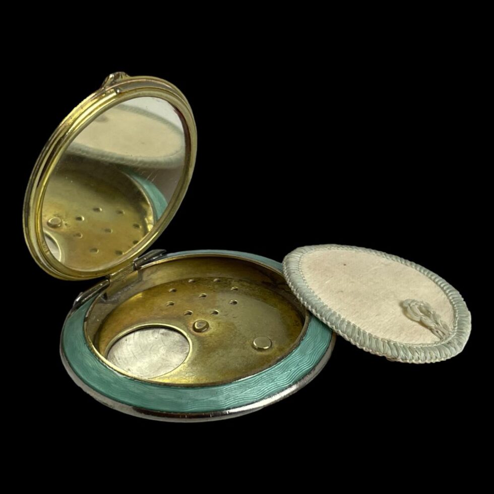 Photo of 1920s compact shown open with the powder pudd removed and put leaning to the side.