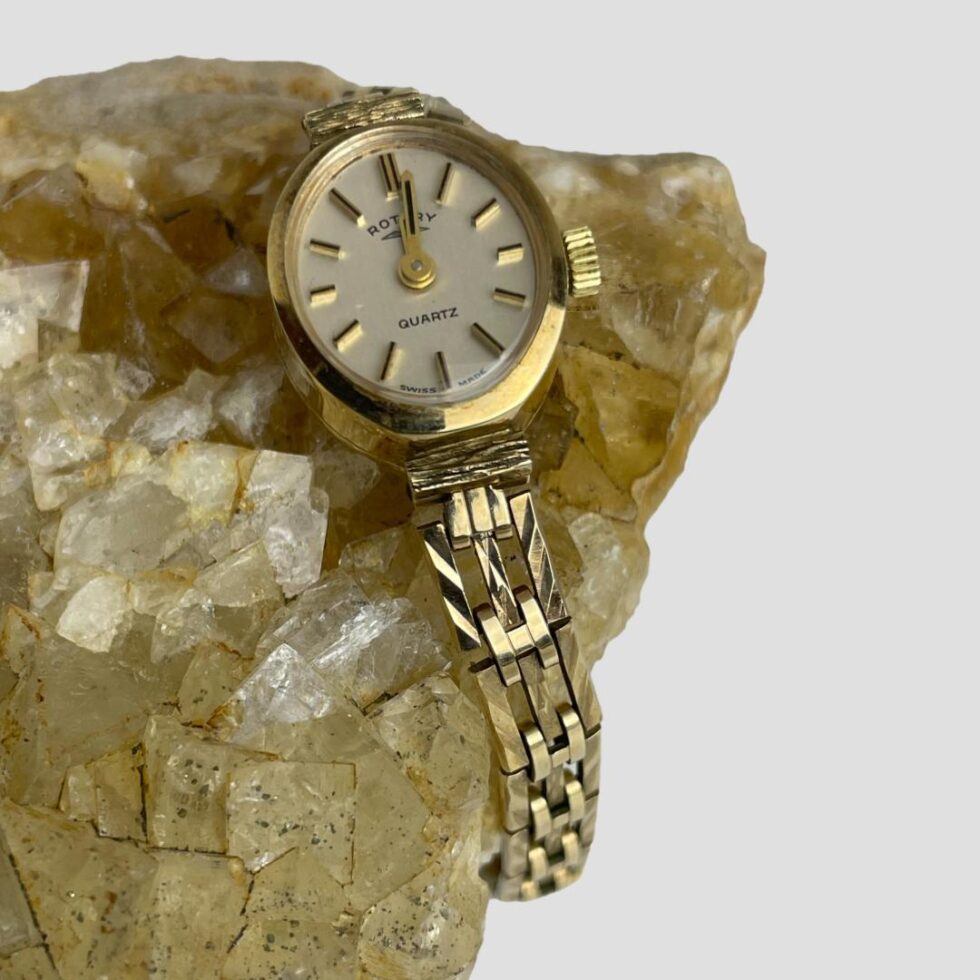 Close up photo of the watch face and lower part of strap. The watch is displayed around a rock of natural river quartz.