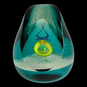 Main photo of Caithness glass druid paperweight displayed with the flat sliced away side on display. The paperweight is a pear shape with a slice taken out from the top along a third of its length. The druid design is a yellow bubble at the centre with a stylised pointed purple druids hat created as a swirl of colour. The main glass is a bright blue almost turquoise colour with a grainy white sand like layer at the bottom. Something very magical about this paperweight.