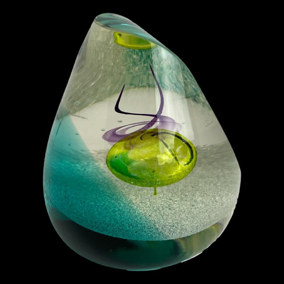 Photo of Caithness glass druid paperweight this time displayed with the flat edged side not visible & facing the top right corner. The colour structure changes again at this angle with a reflection of the yellow bubble just appearing at the top.
