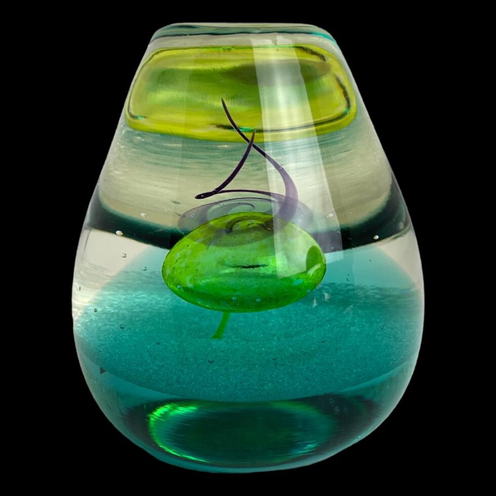 Photo of druid paperweight displayed with the rounded back side on display. More magic! From this angle, the yellow bubble at centre has turned a shade of green and the bubble now appears to be at the top of the glass. This is just one paperweight but can be many!