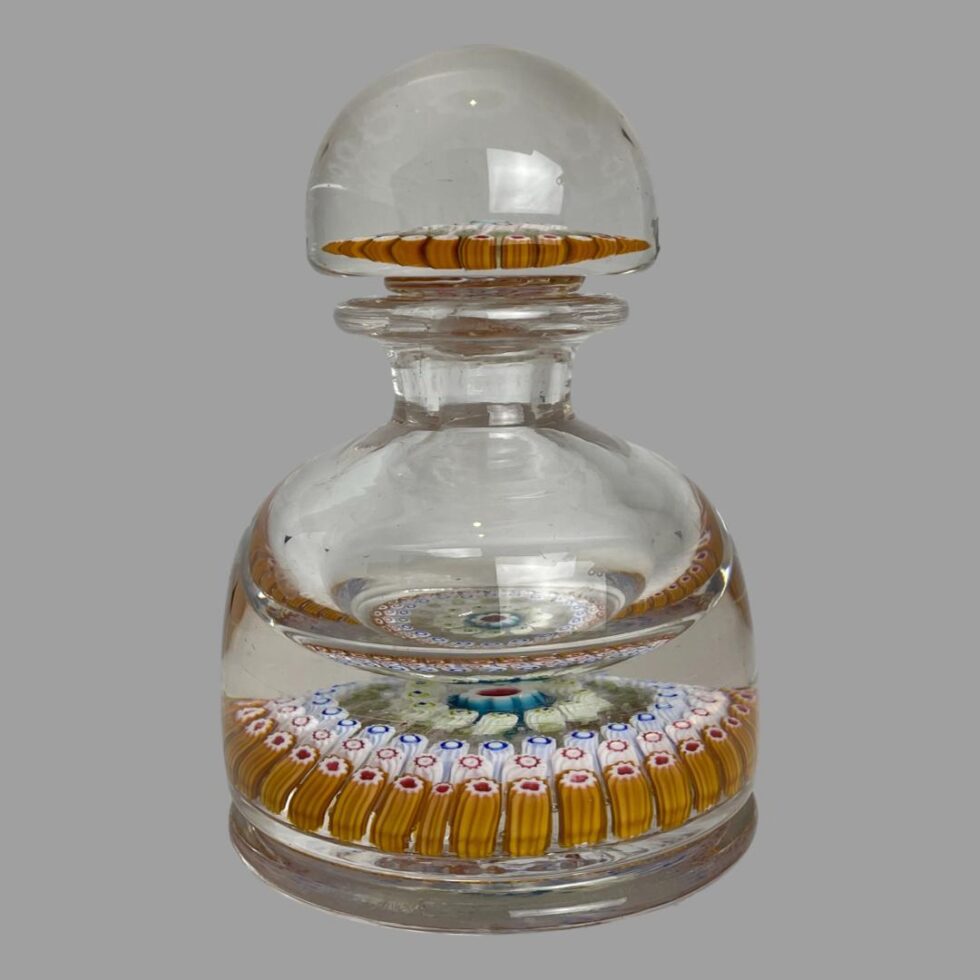 Photo of antique millefiori glass inkwell seen from an eye level with lid in its place. From this angle, it is clear that the ink containing well is just at the top part of the bottle.