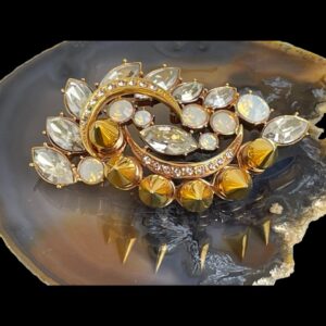 Main photo of Mawi London designer brooch displayed on top of a slice of natural agate. The row of gilt spikes is arched along the bottom in this photo with the crystals leaves scattered around 2 crescent moon shaped details within the brooch. The reflection of the gilt spikes can be seen on the agate. This is a fantastic piece of jewellery!