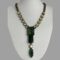 Main photo of Philippe Ferrandis designer necklace displayed on a white coloured display stand with the necklace front forward facing. The long non detachable pendant is a deep green shade like moss agate with a single citrus coloured crystal separating the oval green at bottom from the 2 rectangular green above. 6 citrus coloured crystals line the lower part of the necklace chain to either side followed by a thick brassy coloured chain. The extension chain has a single citrus crystal on the end.