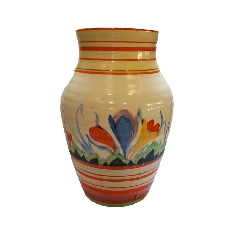 Main photo of Clarice Cliff Bizarre Isis vase shown from an eye level angle with large blue crocus side showing. Other than the single blue crocus the other colours are trademark yellows and oranges. The floral design goes all around the vase. The full name for this design pattern is Bizarre Isis.