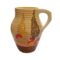 Main photo of Clarice Cliff Bizarre Lotus jug seen from an eye level shown from side with most decoration with handle to the right. The jug has alternating thin stripes in graduating shades of orange and yellow from top to bottom with a thin patch of solid brown around the base. 2 stylised tress - tall like leylandii in yellow to left and brown to right with large flowers in the foreground in yellow and vibrant orange. There are 3 areas on the jug with decoration on.