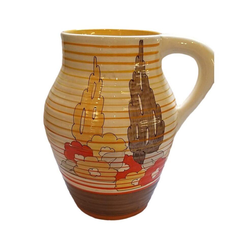 Main photo of Clarice Cliff Bizarre Lotus jug seen from an eye level shown from side with most decoration with handle to the right. The jug has alternating thin stripes in graduating shades of orange and yellow from top to bottom with a thin patch of solid brown around the base. 2 stylised tress - tall like leylandii in yellow to left and brown to right with large flowers in the foreground in yellow and vibrant orange. There are 3 areas on the jug with decoration on.