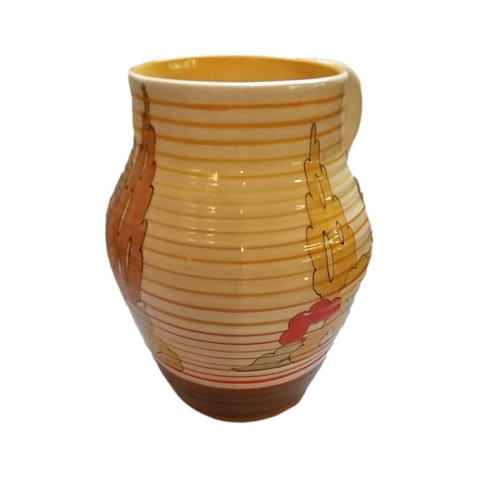 The jug seen mostly from the front (handle can be seen slightly to right in background) This side has no decorations just a little visible of the trees and flowers to left and right.