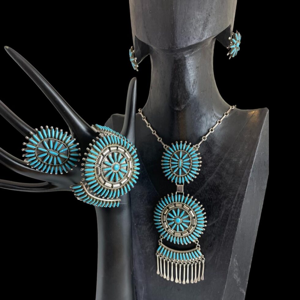 Photo of all pieces displayed on a black wooden display stand and separate hand. The wooden stand has holes for earrings where the earrings are displayed and the necklace is around the neck. The hand with outstretched fingers has the ring on the middle finger with the cuff bracelet hanging below it across the lower part of the hand.