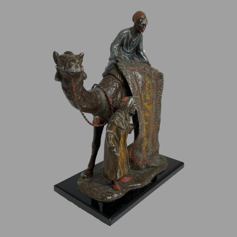 Another angle shot of the rug merchants this time taken from the front end of camel. The camel is looking straight to camera while the seated merchant is looking down towards bottom right and standing merchant is looking to his right.