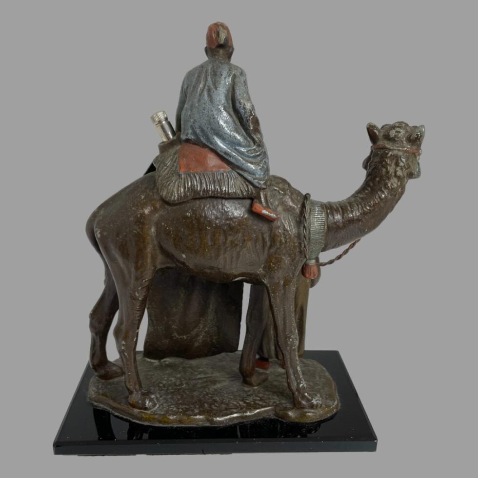 Photo of the opposite side of figurine displaying the camels side and the back of the seated merchant. The striker is sticking out to the left of seated merchant and was probably painted to look like part of the saddle.