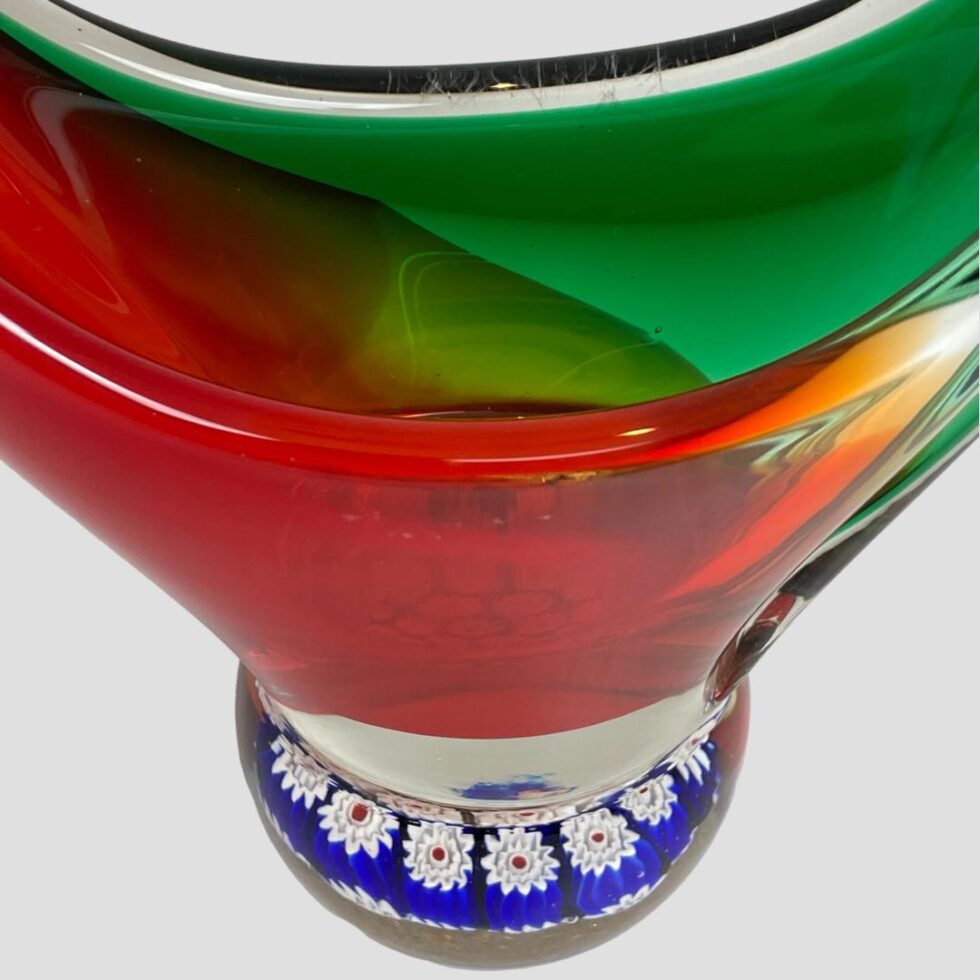 Photo looking down at the central area of the Murano basket showing the vibrant red (foreground) and green (background) glass with the millefiori base in cobalt blue and white flowers protruding at the bottom.