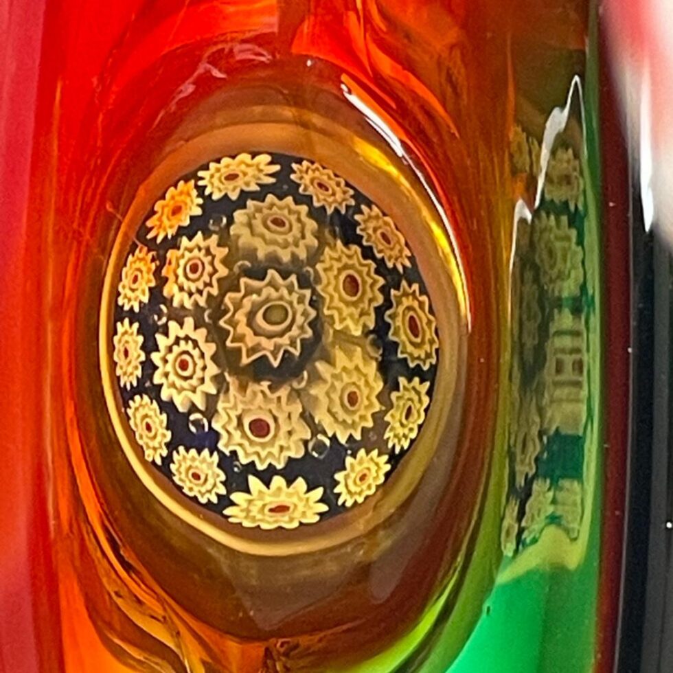 Photo looking down at the millefiori base through the top of the basket. The red glass covers most of the space around with just a little bit of green to the right which is reflecting some of the millefiori.