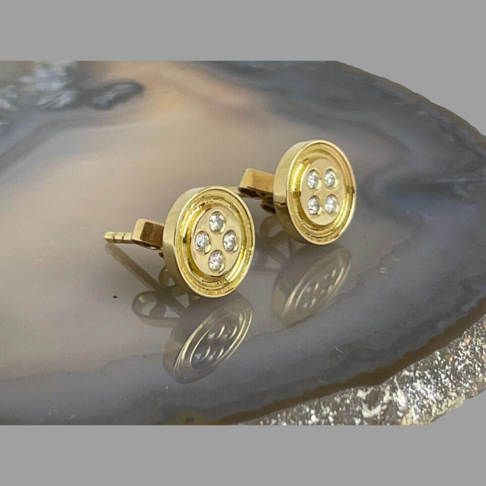 Photo of gold button earrings displayed on top of the slice of natural agate with the earring fronts facing towards the right.