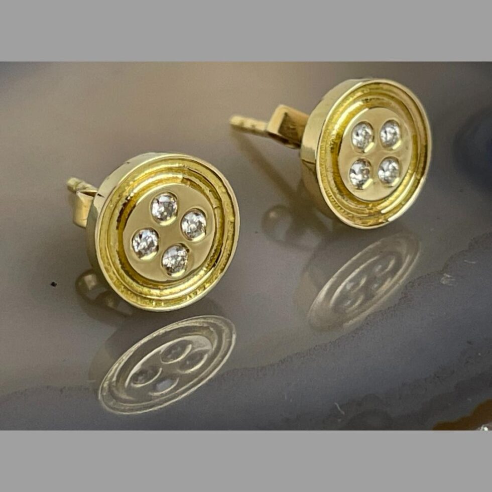 A close up photo of the gold diamond button earrings with front facing towards the bottom right corner. The yare beautifully made and do look just like buttons but in gold...with diamonds where the thread holes should be!