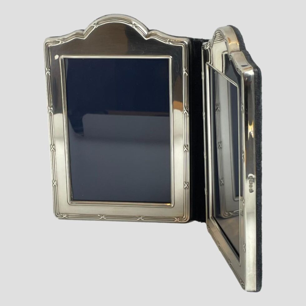 Photo of double silver photo frame seen with one half in the foreground displayed sideways which the hallmark just visible on the side. The other half of the frame is shown facing forward.