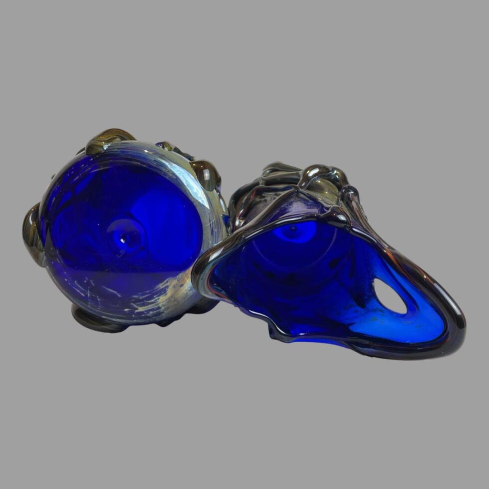 Photo of both signed studio glass vases displayed laid on their side with 2 pointed one on the right looking into the mouth and 3 pointed one looking at the base. The base of the 3 pointed vase is clear blue .