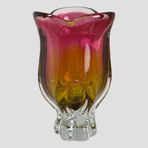 Main photo of Josef Hospodka ruby/amber glass vase seen from an eye level against a light grey background. The vibrant colours of this glass vase is so stunning like a hot fuchsia pink merging into a marmalade orange. (Officially ruby & amber) The shape is a little like a variety of tulip flower head. A vase not requiring flowers as beautiful as it is!