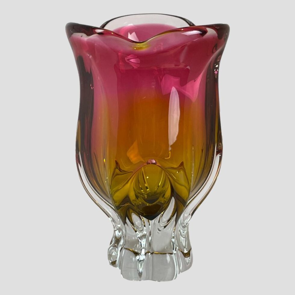 Main photo of Josef Hospodka ruby/amber glass vase seen from an eye level against a light grey background. The vibrant colours of this glass vase is so stunning like a hot fuchsia pink merging into a marmalade orange. (Officially ruby & amber) The shape is a little like a variety of tulip flower head. A vase not requiring flowers as beautiful as it is!