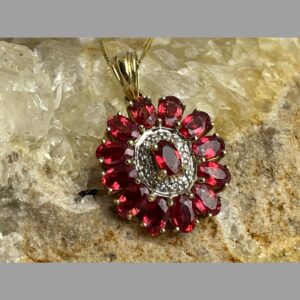 Main photo of ruby diamond pendant &chain displaying just the pendant forward facing and on top of a rock of natural river quartz. The light is shining on the stones which are lit up beautifully.