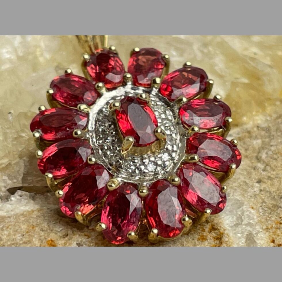 Close up photo of the ruby diamond pendant &chain still displayed on a rock of natural river quartz and the light bouncing off each stone.