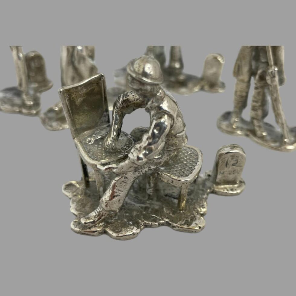 A close up photo of the cane chair repair man seen from a slightly raised angle to show the top of chair. He is seated on a cane topped stool and in mid repair of a chair which has a hole. There is a spanner on the chair. To the right is the milestone which says 12 miles for this particular Victorian worker.