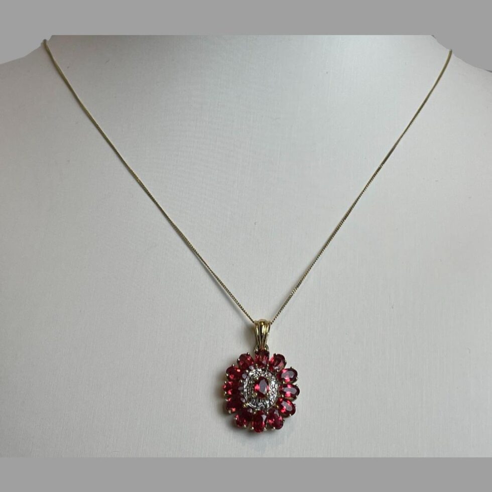 Photo of ruby diamond pendant &chain displayed on an off white display stand and pendant forward facing.